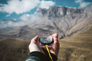 Viewpoint shot. A first-person view of a man's hand holds a compass against the background of an epic landscape with cliffs hills and a blue sky with clouds