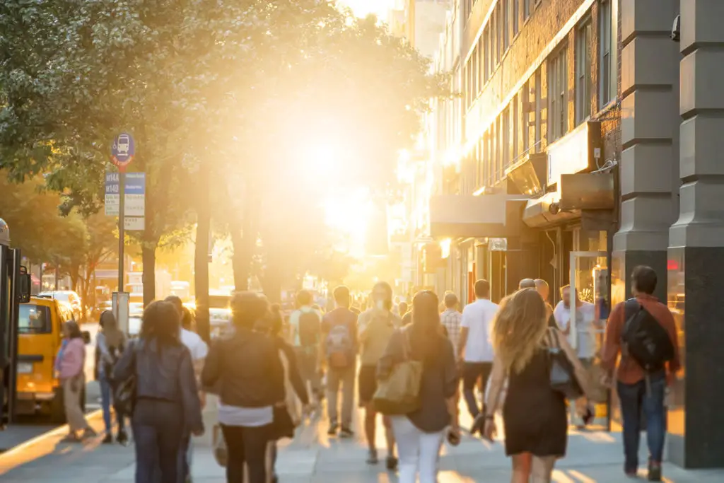 crowds of people walk around on 14th Street in Manhattan, New York City with the glow of sunlight in the background.