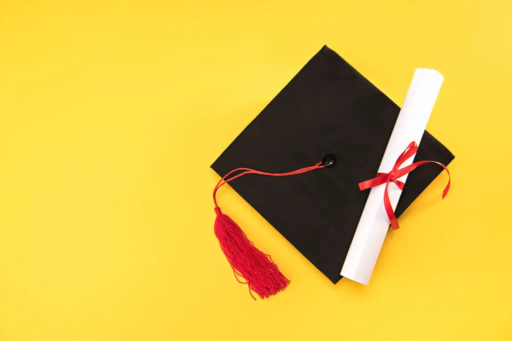 Top view of graduation mortarboard and diploma on yellow background, education concept