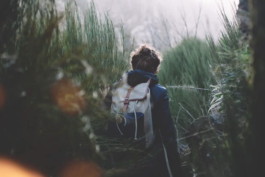 Girl walking among huge grass in mountains with backpack