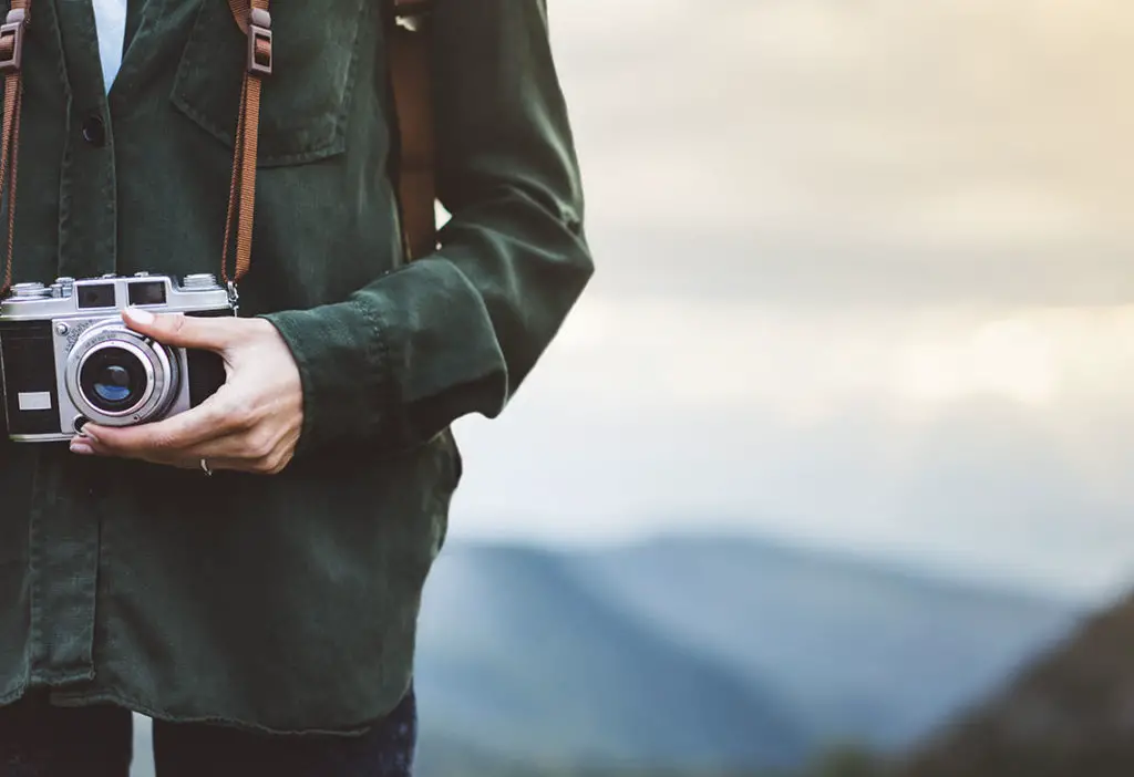 Young girl with bright backpack taking photo of amazing landscape sunset 