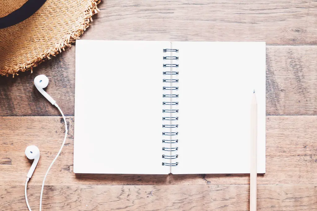 Blank notebook, earphones and hat on wooden table