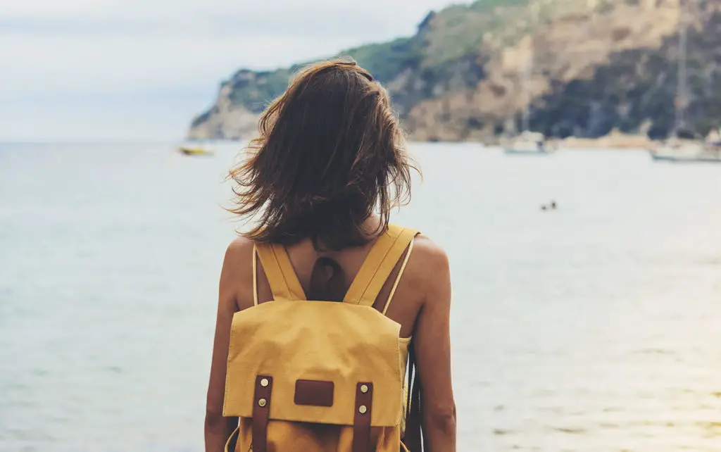 girl with backpack in sand coastline on nature landscape