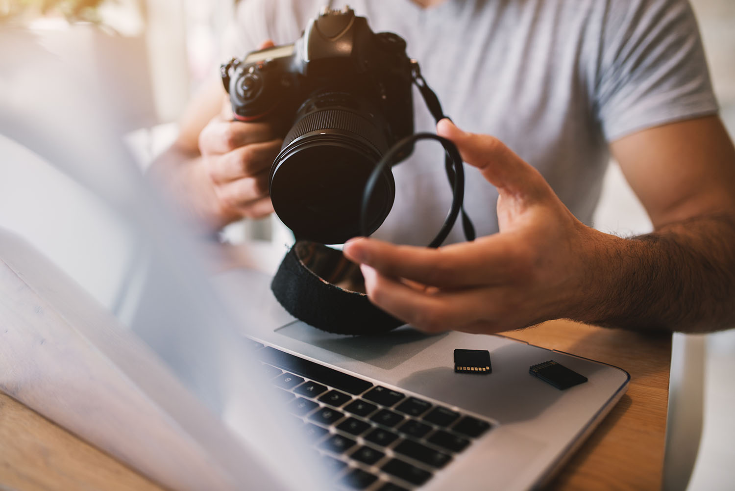 Man taking off lens of a professional camera while using a laptop.