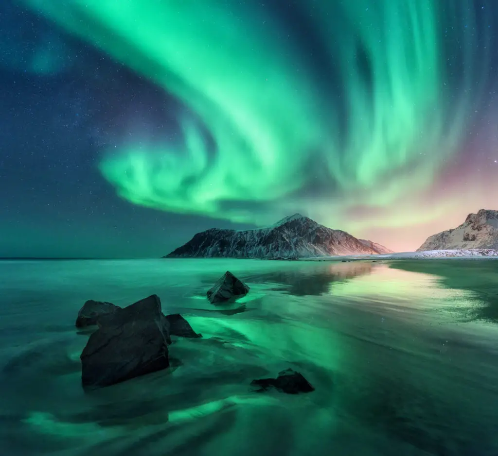 Aurora. Northern lights in Lofoten islands, Norway. Sky with polar lights, stars. Night winter landscape with aurora, sea with sky reflection, stones, sandy beach and mountains. Green aurora borealis